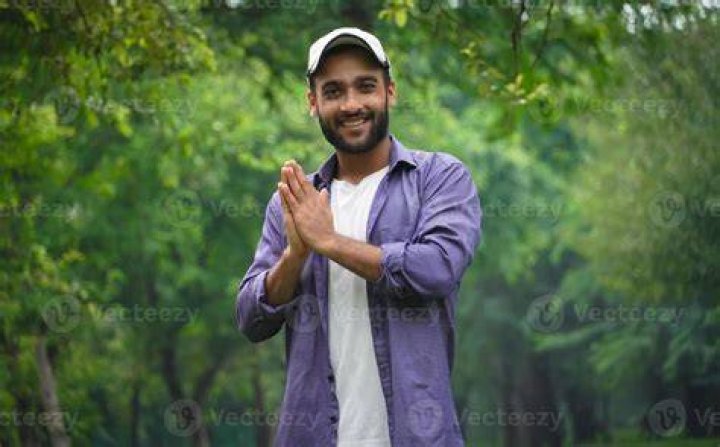 He is doing a Namaste as he is standing in front of a Hindu temple.